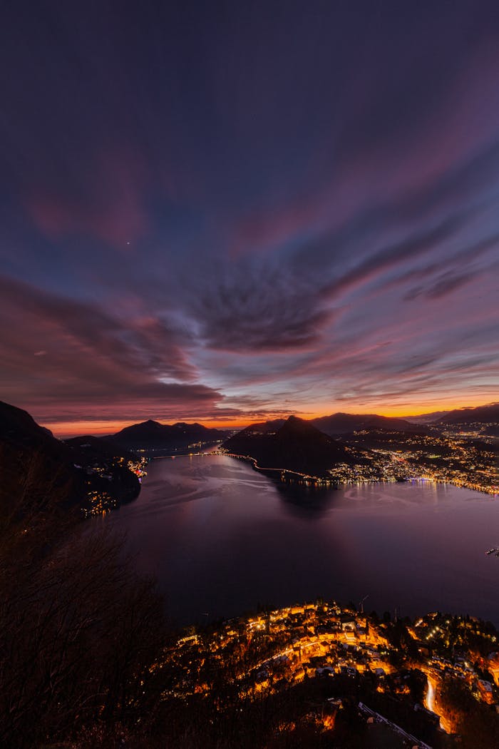 Stunning aerial view of Lugano's illuminated bay and cityscape at sunset.