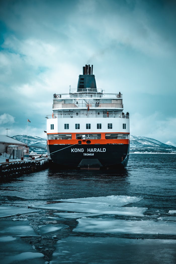 Majestic ferry Kong Harald docked at Finnsnes with icy waters and snowy mountains in view.